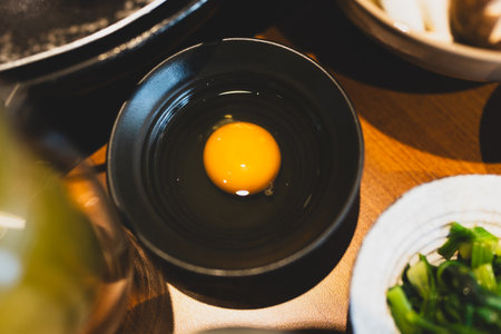A raw egg yolk in a black bowl. Raw egg as sauce for hotpotの写真素材
