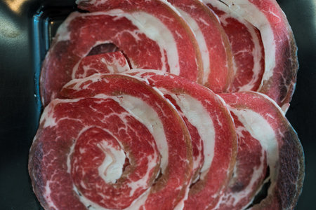A close up shot of sliced raw meat, arranged on a plate, ready to be cooked in a hot pot