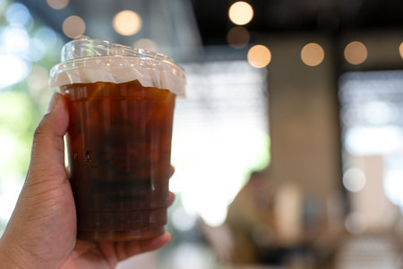 Hand holding plastic cups of delicious iced americano coffee