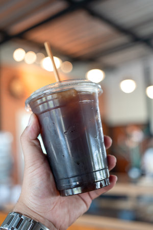 Hand holding a plastic cup filled with iced americano coffee and a straw.の写真素材