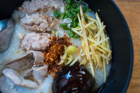 Congee with minced pork, pork offal, fried garlics minced pork and preserved egg in a black bowl. Asian breakfast.の写真素材