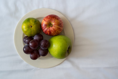 A plate of grapes, a lime, and a red and green apple on white plate sitting on a bed at a resort