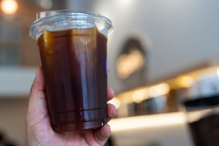 Close up of a hand gripping a glass of cold black coffee with a cafe