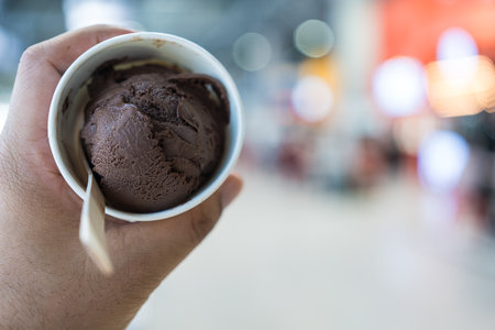 Indulgent chocolate ice cream scoops in a paper cup on man hand.の写真素材
