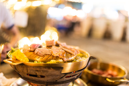 Mookata, Thai BBQ grill pork dish. The round hot pan with pork is grilled on top. Flavorful dish for sharing.の写真素材