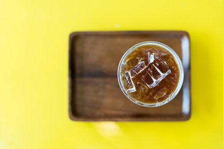A top view of a glass filled with iced black coffee, glistening with ice cubes under light.
