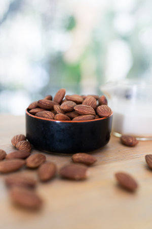 Almonds in a black bowl and a glass of almond milk on wood table