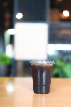 Refreshing iced Americano coffee in plastic cup on wood table