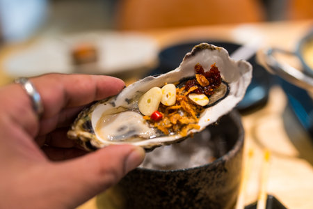 Fresh Oyster in shell in hand that topping with fried shallot, garlic and chili paste eating with Thai style seafood sauce.の写真素材