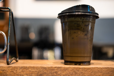 Iced mocha in a black cup with black lid on wood tableの写真素材
