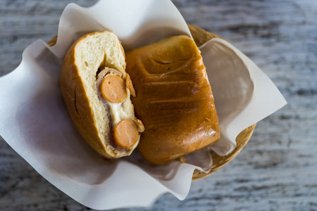 Bread stuffed smoked pork sausage and cheese with dressing mayonnaise sauce on paper in basketの写真素材