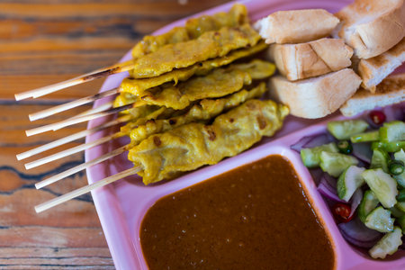 Thai satay skewers with grilled pork served with toasted bread and dipping sauces served on pink plate, Thai food styleの写真素材
