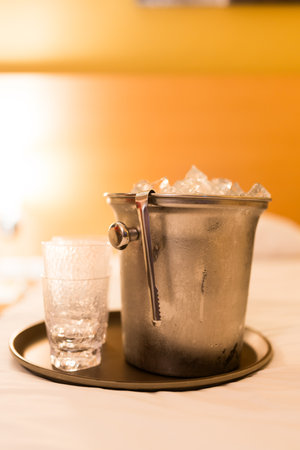 A bucket with ice and empty glass placed on a white bed in a luxury hotelの写真素材