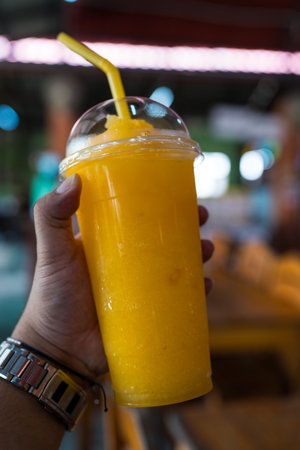 Orange smoothie in plastic glass on man handの写真素材