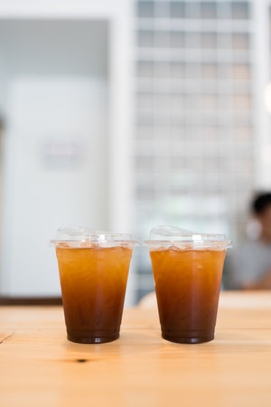 Two glasses of iced black coffee on wood table.