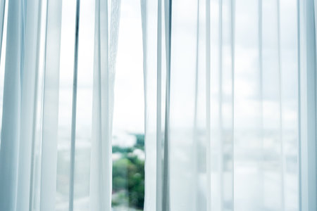 Elegant white sheer curtains allow soft sunlight to filter into a serene room, creating a bright and peaceful home interior atmosphere.の写真素材