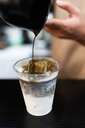 Man making ice charcoal latte in a clear plastic cup showing the texture and refreshing look of the drinkの写真素材