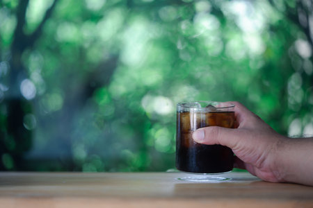 Chilled fizzy cold drink in glass with ice cubes on handの写真素材