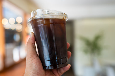 Hand holding iced black coffee or americano coffee in plastic cup,