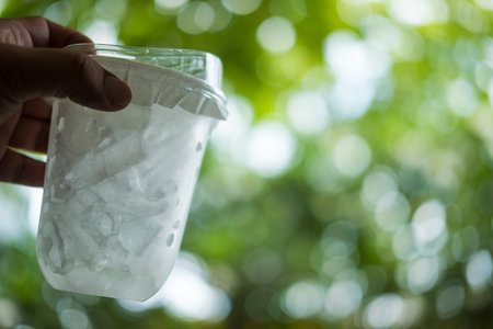 Plastic transparent cup of ice drink with lid on hand against nature backgroundの写真素材