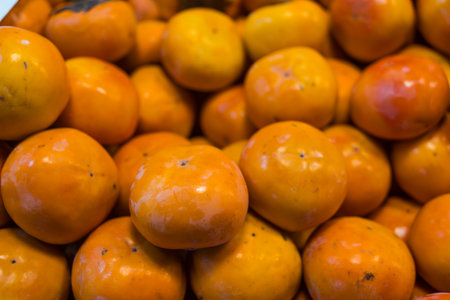 Freshly harvested ripe orange persimmons piled up at a market stall, showing their smooth skin and calyx.の写真素材