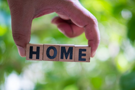 HOME word on wooden cubes, letters on wooden cubes in hand against nature backgroundの写真素材