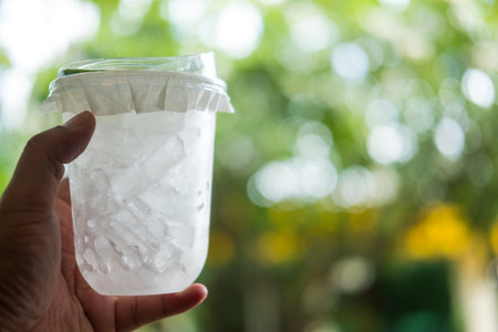 A plastic cup filled with ice with lid on hand against nature backgroundの写真素材