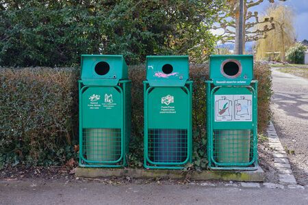On a street there are 3 green recycling bins on a hedge