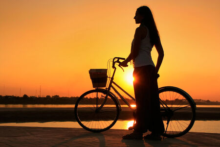 Silhouetted woman with bicycle at Mekong river waterfront sunset in Vientiane, Laosの写真素材