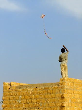 Indian boy flying kite from the roof of traditional house in Thar desert near Jaisalmer, Rajasthan, India. Thar desert forms a natural boundary between India and Pakistanの写真素材