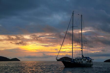 Silhouetted tourist sailboat at sunrise anchored near Chinese Hat island in Galapagos National Park, Ecuadorの写真素材