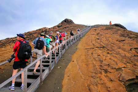 Group of tourists walking on a boardwalk on Bartolome island, Galapagos National Park, Ecuador. The island consists of an extinct volcano and a variety of red, orange, green, and glistening black volcanic formations.のeditorial素材
