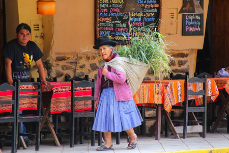 Local woman walking with keperina full of grass in the street of Ollantaytambo, Peru. Ollantaytambo...