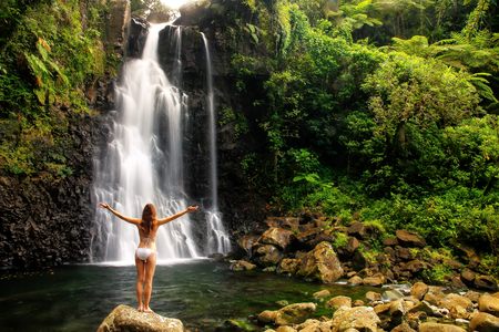 Young woman in bikini standing by Middle Tavoro Waterfalls in Bouma National Heritage Park on Taveuni Island, Fiji. Taveuni is the third largest island in Fiji.の写真素材