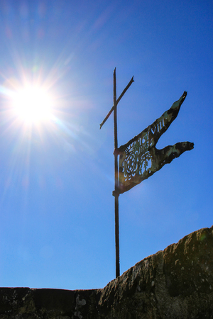 Metal flag on the top of Montalcino Fortress tower against blue sky with sunburst, Val d'Orcia, Tuscany, Italy. The fortress was built in 1361 atop the highest point of the town.の写真素材