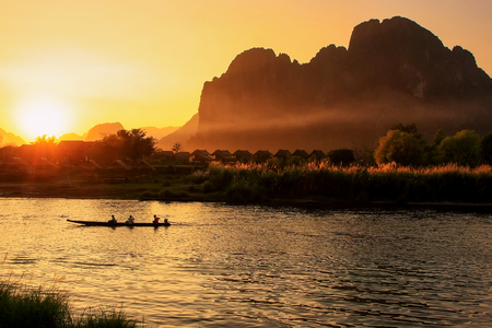 Sunset over Nam Song River with silhouetted rock formations and a boat in Vang Vieng, Laos. Vang Vieng is a popular destination for adventure tourism in a limestone karst landscape.のeditorial素材