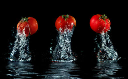 three tomatos splashing out of water with water reflect on black backgroundの写真素材