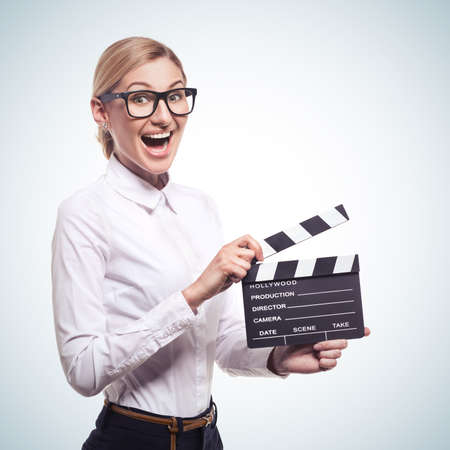 Attractive young woman holding clapper board in her hands isolatad on blue gradient backgroundの写真素材