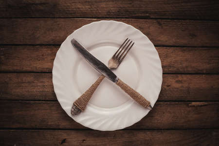 White shiny plate with folk and knife on wooden tableの写真素材