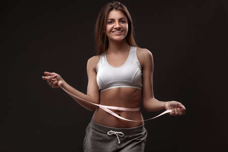 Sporty woman with measurment tape on dark grey backgroundの写真素材