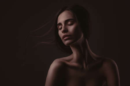 lowkey portrait of beautiful woman with closed eyes over dark backgroundの写真素材