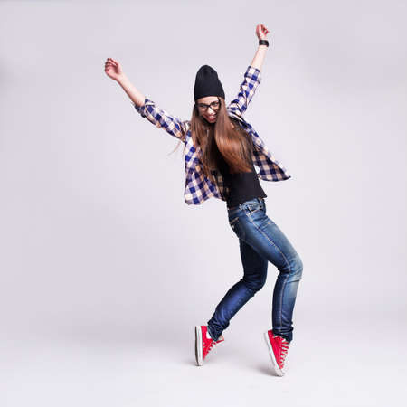 Dancing hipster girl in glasses and black beanie on the wooden backgroundの写真素材
