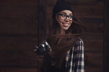 Hipster smiling girl in glasses and black beanie with vintage camera on the wooden backgroundの写真素材