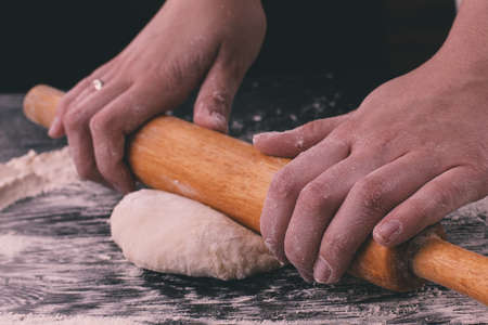 Close up homemade cooking, female hands roll out pastry with rolling-pin on wooden tableの写真素材