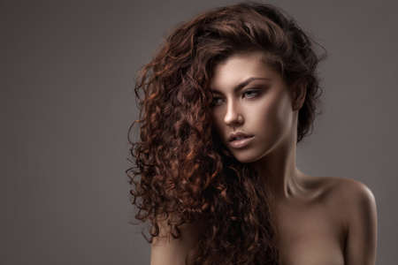 studio shot of woman with healthy brown curly hair isolated over grey backgroundの写真素材