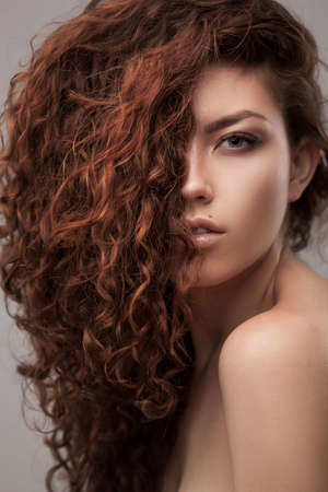 studio shot of woman with healthy brown curly hair isolated over grey backgroundの写真素材
