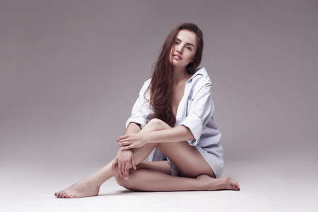 fashion portrait of a beautiful sexy woman with long hair in white shirt sitting on light grey backgroundの写真素材