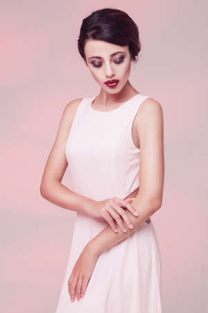 portrait of beauty woman in white dress isolated over light pink studio backgroundの写真素材