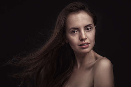 Beautiful woman  with long hair and freckles on dark studio backgroundの写真素材