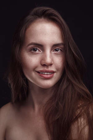 smiling woman with long hair and freckles on dark studio backgroundの写真素材